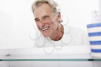 Senior Man Looking At Reflection In Bathroom Mirror