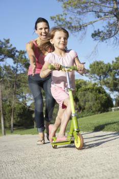 Mother Teaching Daughter To Ride Scooter In Park