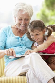 Grandmother And Granddaughter Reading Book On Garden Seat