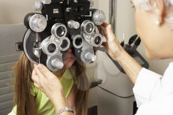 Female Optician In Surgery Giving Girl Eye Test
