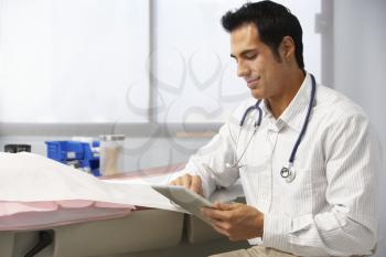 Male Doctor In Surgery Using Digital Tablet