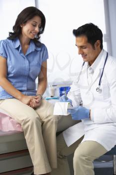 Doctor In Surgery With Female Patient Writing Prescription