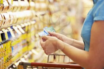 Woman In Grocery Aisle Of Supermarket With Coupons