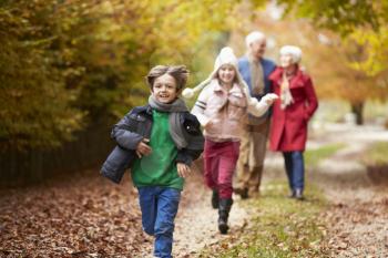 Grandparents With Grandchildren Running Along Autumn Path