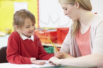 Teacher Helping Female Pupil With Practising Writing At Desk