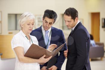 Three Consultants Discussing Patient Notes In Hospital