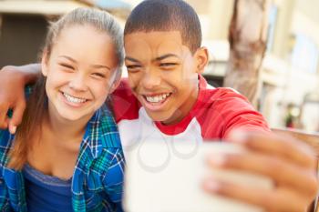 Teenage Couple Sitting On Bench In Mall Taking Selfie