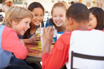 Group Of Children In Caf Looking At Text On Mobile Phone