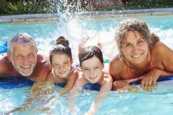 Grandparents With Grandchildren On Airbed In Swimming Pool
