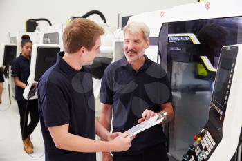 Male Apprentice Working With Engineer On CNC Machinery