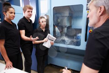 Three Apprentices Working With Engineer On CNC Machinery