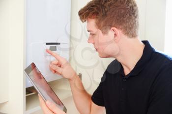 Young technician servicing a boiler, using tablet computer