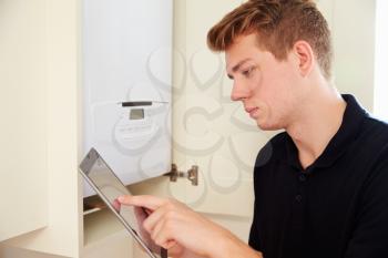 Young technician servicing a boiler, using tablet computer
