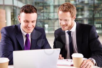Two young businessmen having coffee, using a laptop computer