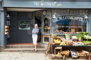 Female Owner Standing Next To Produce Display At Deli