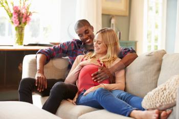 Pregnant Couple At Home Relaxing On Sofa Together