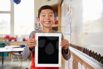 Portrait of elementary school boy holding up tablet computer