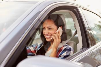 Happy Hispanic female driver using phone in a car