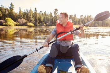 Man Wearing Life Preserver Rowing Kayak On Lake