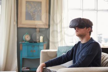 Man Sitting On Sofa At Home Wearing Virtual Reality Headset
