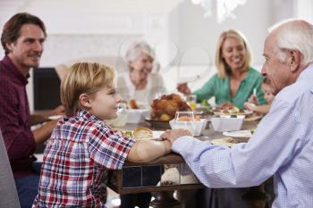 Extended Family Group Sit Around Table Eating Meal At Home