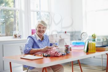 Senior Woman Making Clothes Using Sewing Machine At Home