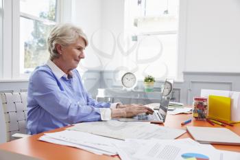 Senior Woman Sits At Desk And Works On Laptop In Home Office
