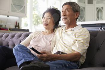 Senior Asian Couple At Home On Sofa Watching TV Together