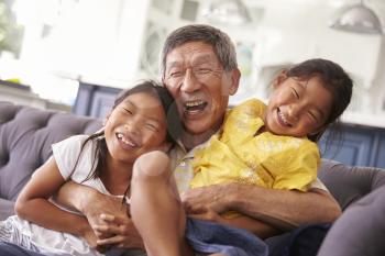 Grandfather And Granddaughters Relaxing On Sofa At Home