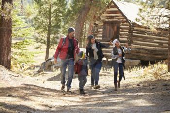 Family walking on forest path past a log cabin