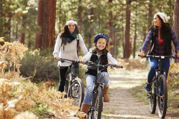 Lesbian couple cycling in a forest with their daughter