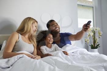 Mixed race couple and daughter watching TV in bed together
