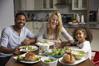 Girl and mixed race parents dine in their kitchen, to camera