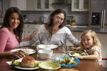 Female gay couple and daughter dining at home look to camera