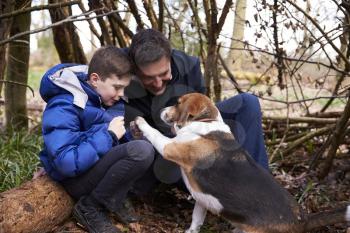 Father and son playing with dog under a shelter of branches