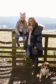 Mother and daughter by a country gate with pet dog, vertical