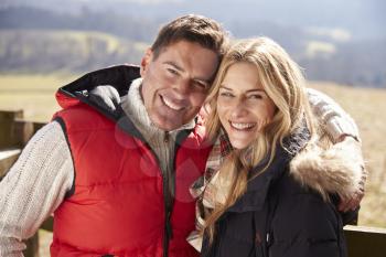 Couple in coats embracing in the countryside look to camera