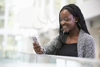 Young black female student using phone in university foyer