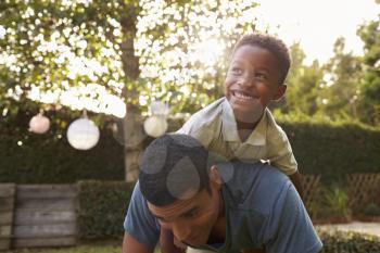 Young black boy playing on his dads back in a garden
