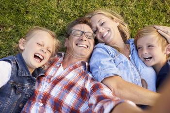 White family lies on grass taking selfie, camera out of shot
