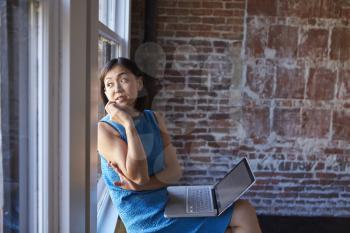 Businesswoman In Office Sitting By Window Using Laptop