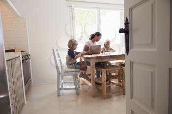 Mum and two kids working at kitchen table, seen from doorway