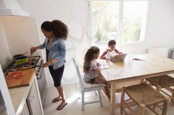 Mum cooking while kids work at kitchen table, elevated view