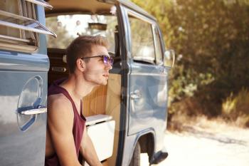 Young man sitting in the open doorway of a camper van