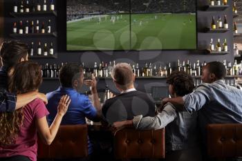 Rear View Of Friends Watching Screen In Bar Together