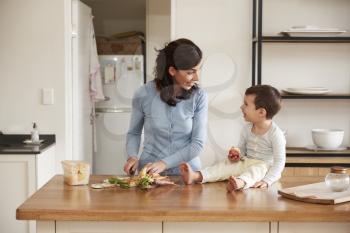 Son Helping Mother To Prepare Food On Kitchen Island