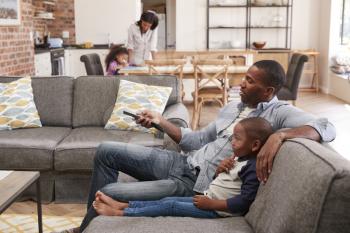 Father And Son Sit On Sofa In Lounge Watching Television