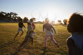 Elementary school kids playing football in a field, back view