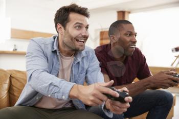 Two Male Friends Sitting On Sofa In Lounge Playing Video Game