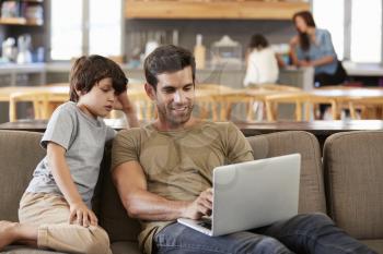 Father And Son Sitting On Lounge Sofa Using Laptop Together